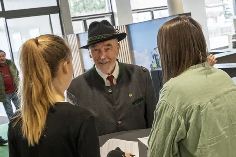 Ein Mann mit Hut wird in der Eingangshalle von zwei Mitarbeiterinnen begrüßt, die mit dem Rücken zur Kamera stehen.