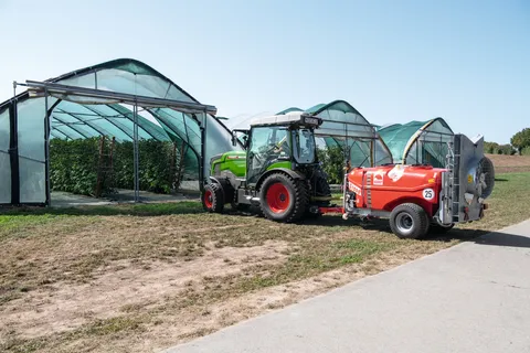 Ein Fendt e100 V Vario fährt in einen Obsttunnel mit Himbeerpflanzen