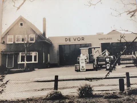 Historische schwarz-weiß Aufnahme von einem Haus mit angeschlossener Werkstätte und landtechnischen Maschinen im Vordergrund, der erste Händlerstandort von de Vor in den 1950er Jahren