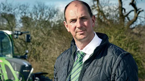 Ein Mann schaut in die Kamera, im Hintergrund ein grüner Fendt Traktor