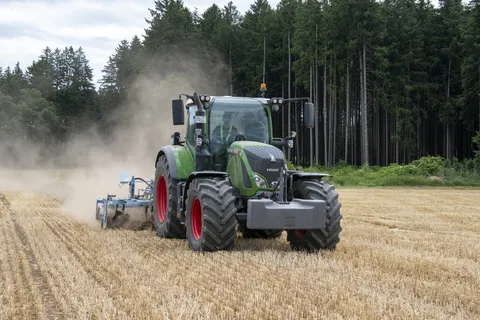 Ein grüner Fendt Traktor fährt mit einem Anbaugerät über ein Stoppelfeld