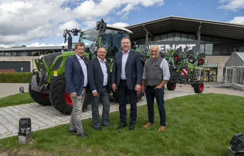 4 Männer stehen vor einem grünen Fendt Traktor und schauen in die Kamera. 3 tragen Hemden, Jeans und ein Jackett, während der andere (rechts) Hemd, Jeans und Weste trägt.