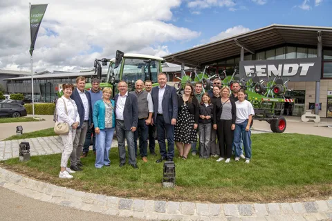 Menschen stehen vor einem grünen Fendt Traktor und schauen in die Kamera. Neben ihnen befindet sich ein Gebäude mit großem Fendt Schriftzug