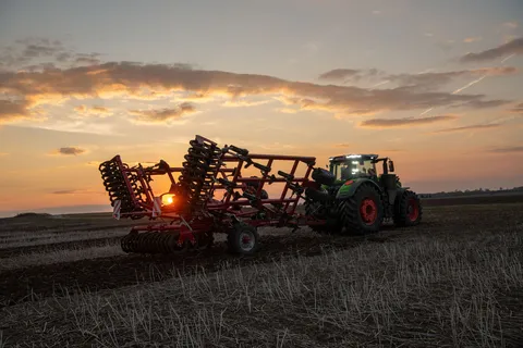 Ein grüner Fendt 1000 Vario fährt mit einem Grubber auf den Acker