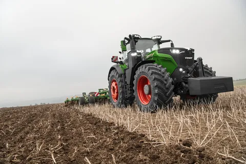 Ein grüner Fendt 1000 Vario mit großen Reifen fährt auf einem Stoppelfeld entlang.