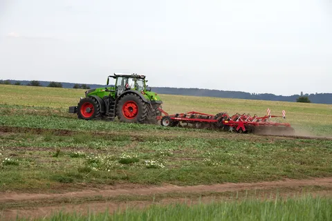 Ein grüner Fendt Traktor 1000 Vario bearbeitet mit einem roten Horsch Grubber ein Feld mit Zwischenfrucht.