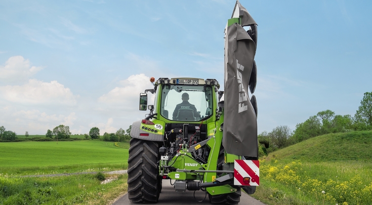 Ein Fendt Vario fährt auf einer Straße und transportiert das Mähwerk in einem 90 Grad Winkel an seinem Heck.