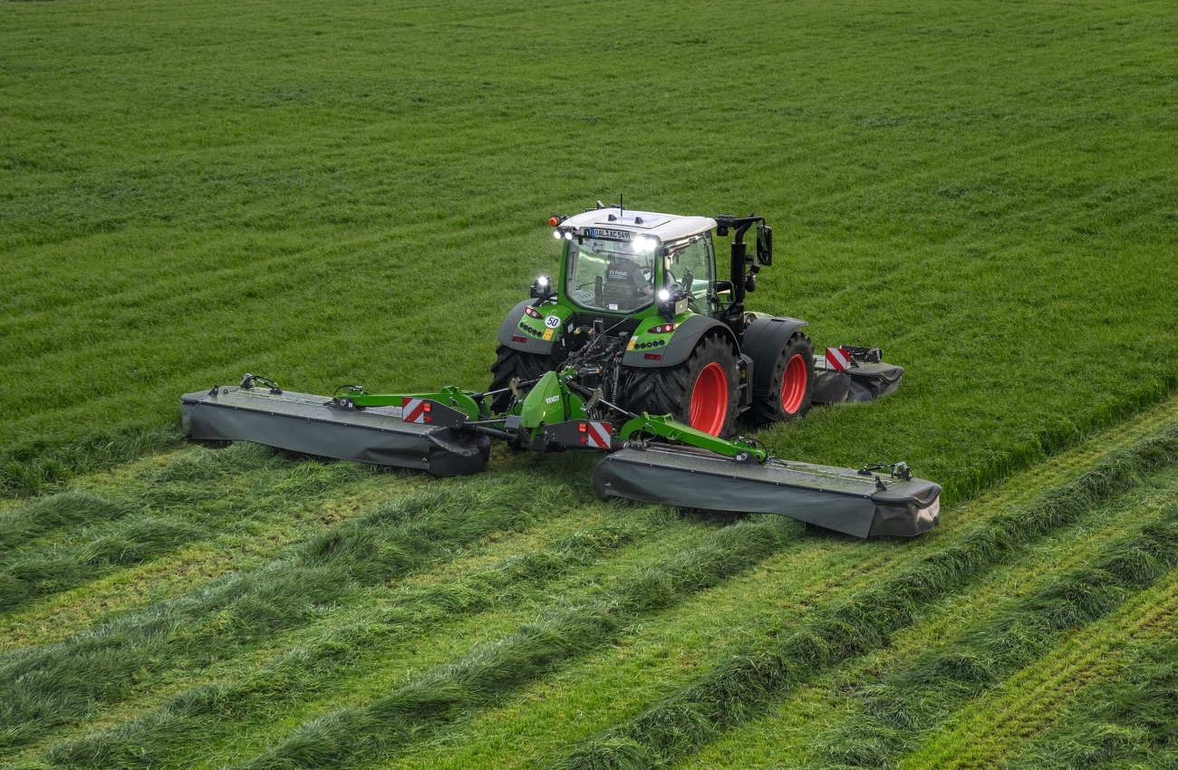 Fendt Traktor mäht bei eingeschaltetem Licht mit Fendt Slicer Front-Heckmähwerkkombination über Wiese