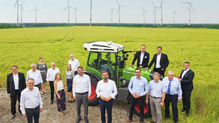 Fendt e100 Vario steht hinter einer Gruppe von Menschen mit Hintergrund von Windkraftwerken