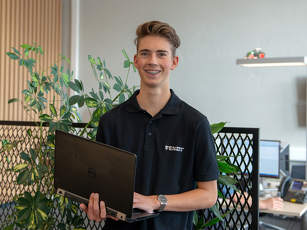 Der Auszubildende steht in einem Büro und hält einen Laptop in der Hand