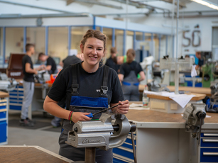 Die Auszubildende zur Fachkraft für Metalltechnik bearbeitet ein Stück Metall in der Lehrwerkstatt