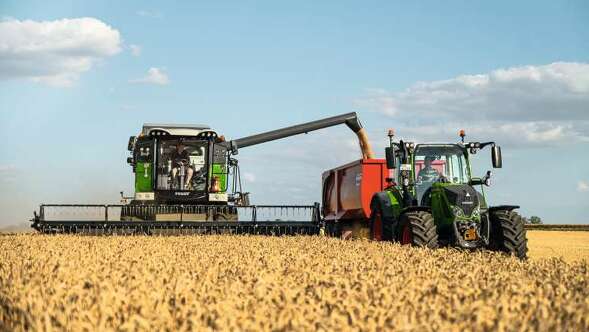 Ein Fendt CORUS und ein Fendt Traktor mit Kipper beim Dreschen.