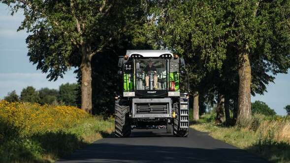 Ein Landwirt fährt mit dem Fendt CORUS 500 auf der Straße durch eine Alee