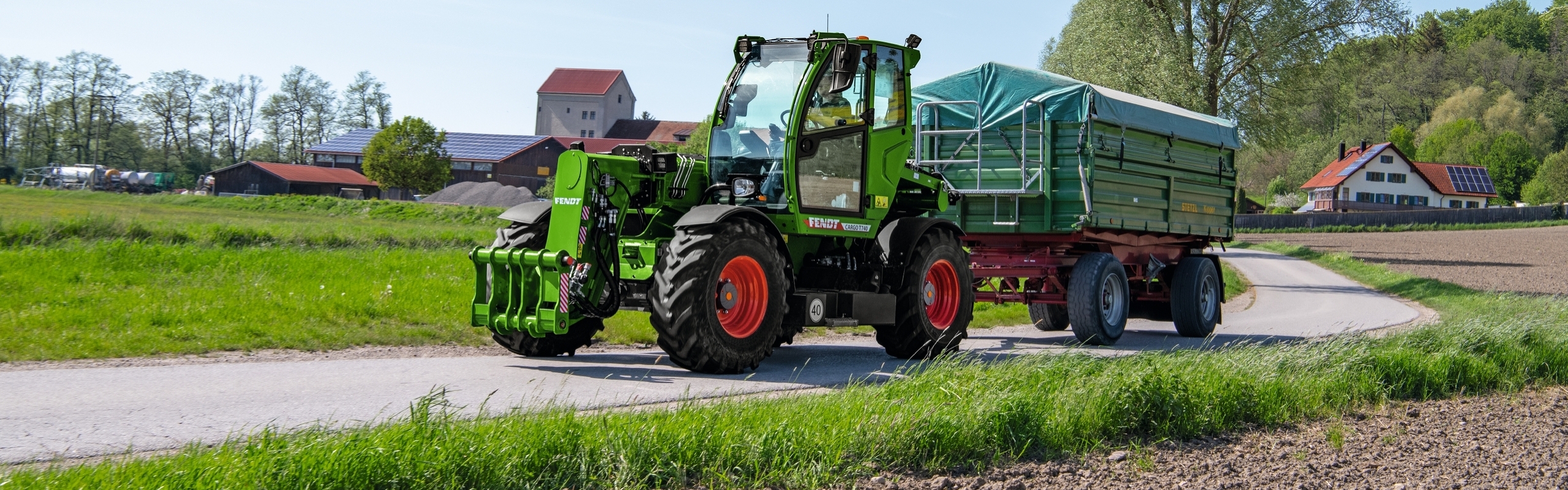 Der Fendt Cargo T740 mit Ladewagen fährt auf einer Landstraße