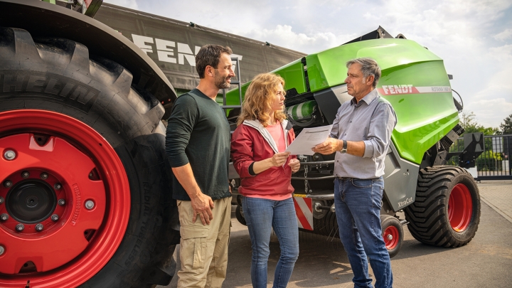 Ein Fendt Händler auf seinem Firmengelände mit einem Landwirtsehepaar im Vertriebsgespräch