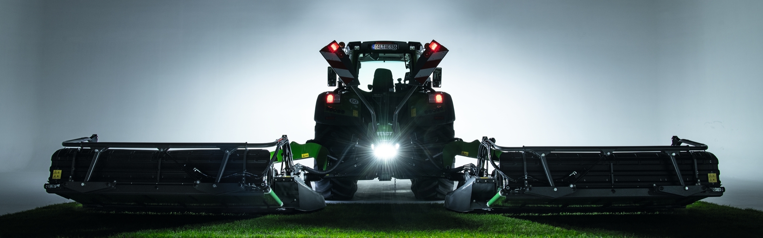 Ein Fendt Traktor steht mit einem Fendt Slicer Scheibenmähwerk in der Abenddämmerung auf einem Feld.