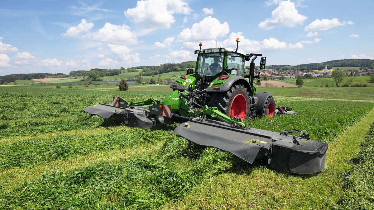 Ein Fendt 700 Vario Gen7 beim Mähen auf der Wiese mit Front- und Heckmähwerk von Fendt.