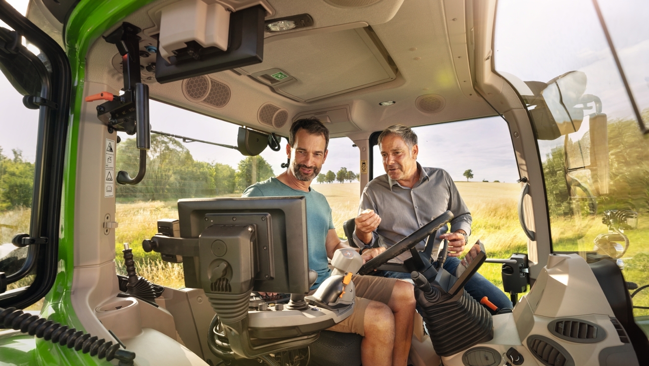 Ein Fendt Händler sitzt mit einem Landwirt auf einem Traktor und erklärt das Terminal.