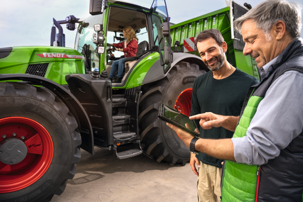 Fendt 700 Vario Produktvorführung Eine Landwirtin sitzt auf einem Fendt 700 Vario Gen7 während ihr Mann sich vor dem Traktor von einem Fendt Händler mit Tablet in der Hand beraten lässt.