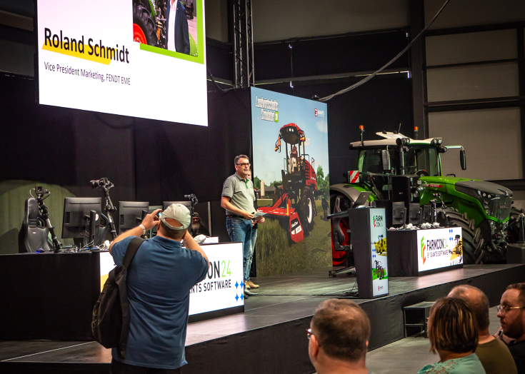 Roland Schmidt, Vice President Fendt Marketing, auf der FarmCon 24 Bühne bei der Begrüßung der FarmCon Besucher Roland Schmidt, Vice President Fendt Marketing EME, steht auf der FarmCon24 Bühne vor den Besucherinnen und Besuchern und begrüßt diese im Fendt Forum, im Hintergrund steht ein Fendt Traktor