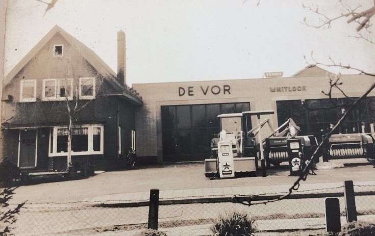 Bild des ersten Händlerstandortes von de Vor in den 1950er Jahren Historische schwarz-weiß Aufnahme von einem Haus mit angeschlossener Werkstätte und landtechnischen Maschinen im Vordergrund, der erste Händlerstandort von de Vor in den 1950er Jahren