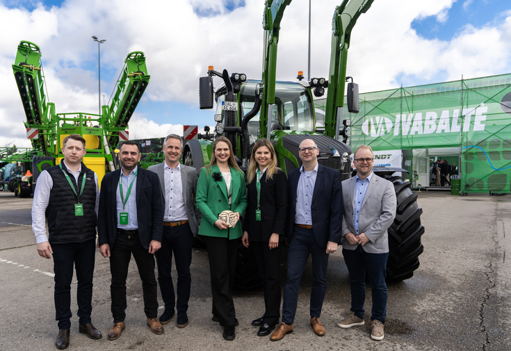 Fendt 620 Vario erhält Innovationspreis in Litauen 7 Menschen, in der Mitte Frauen, eine Frau mit grünem Blazer hält einen Preis in der Hand, vor einem grünen Fendt Traktor