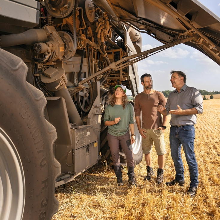 Ein Fendt Händler erklärt einem Landwirtehepaar auf einem Feld, wie der Fendt Mähdrescher funktioniert.