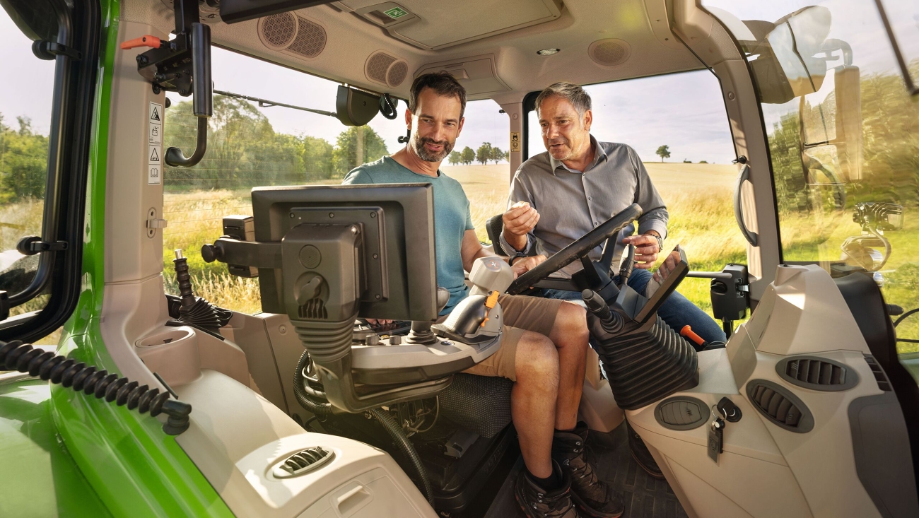 Ein Fendt Händler in der Kabine eines grünen Traktor-Vorführmodells von Fendt bei einem Landwirtskunden auf dem Gelände