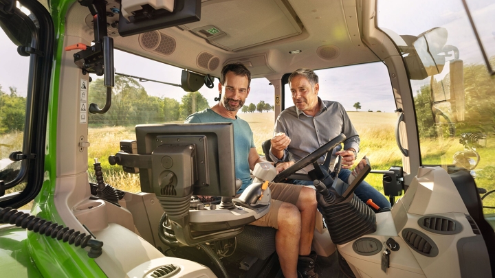 Ein Fendt Händler in der Kabine eines grünen Traktor-Vorführmodells von Fendt bei einem Landwirtskunden auf dem Gelände