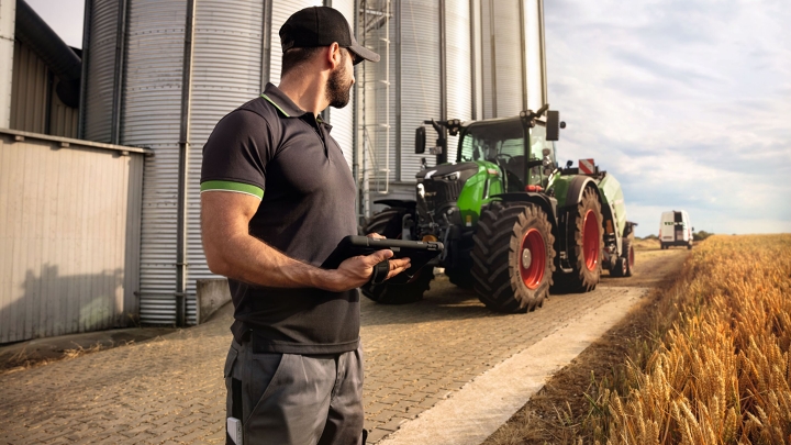 Ein Fendt Service-Techniker schaut auf einen Fendt Traktor 700 Vario Gen6 am Feldrand