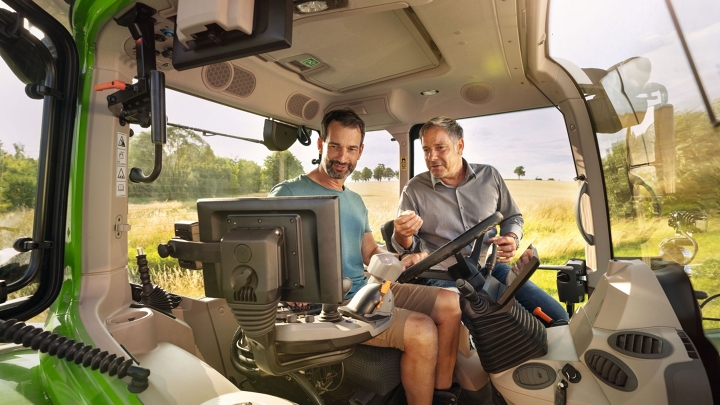 Ein Fendt Händler in der Kabine eines grünen Traktor-Vorführmodells von Fendt bei einem Landwirtskunden auf dem Gelände