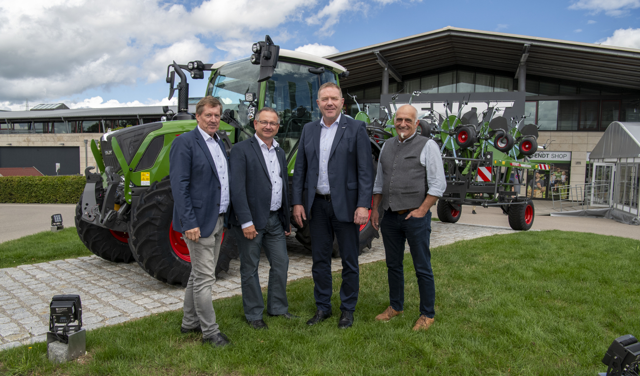 4 Männer stehen vor einem grünen Fendt Traktor und schauen in die Kamera. 3 tragen Hemden, Jeans und ein Jackett, während der andere (rechts) Hemd, Jeans und Weste trägt.