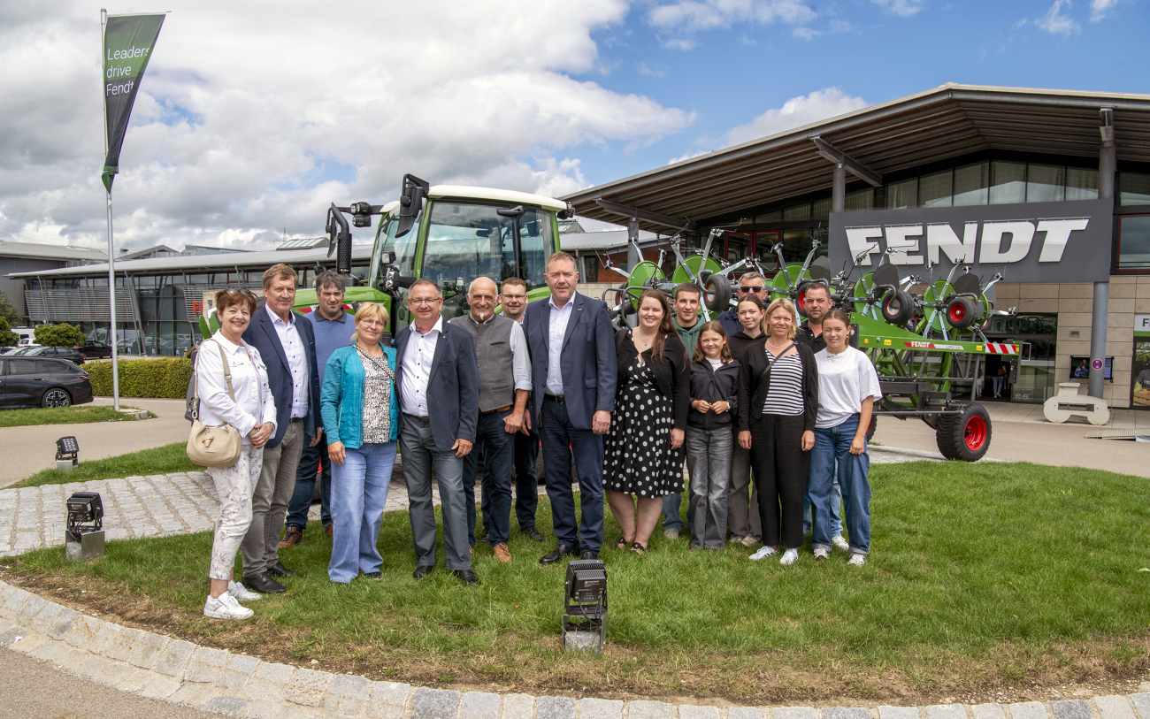 Menschen stehen vor einem grünen Fendt Traktor und schauen in die Kamera. Neben ihnen befindet sich ein Gebäude mit großem Fendt Schriftzug