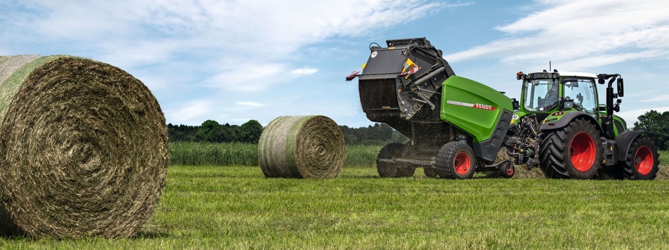 Fendt Rundballenpresse Rotana 160 V Auf einem Feld fährt ein Fendt Traktor mit angehängter Fendt Rundballenpresse Rotana 160 V am Horizont, davor zwei fertig gepresse Rundballen