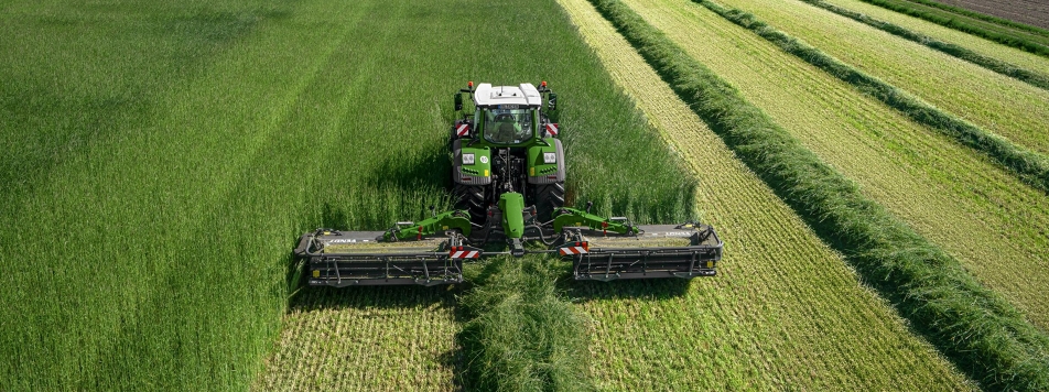 Fendt Slicer 960 KCB Pro Ein Fendt Traktor mit Fendt Slicer 960 KCB Pro Mähkombination auf einer Wiese beim Mähen aus der Vogelperspektive.