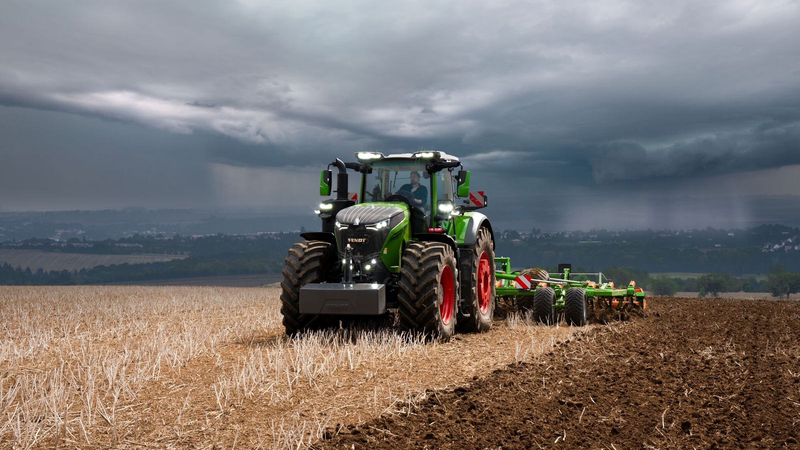 Vor schweren, heraufziehenden Gewitterwolken in der Ferne erledigt der Fendt 1000 Vario Traktor noch kraftvoll seine Feldarbeit