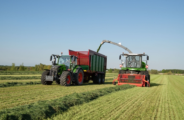 Ein Fendt 500 Vario mit Abschiebewagen und dem Fendt Katana im Einsatz Ein grüner Fendt 500 Vario zieht einen Abschiebewagen von Strautmann neben einem grünen Häcksler von Fendt. Dieser häckselt Gras.