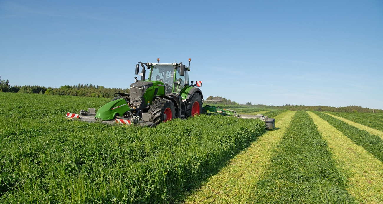 Ein grüner Fendt 724 Vario Gen7.1 mäht mit einem Fendt Slicer Front- und Heckmähwerk eine Wiese.