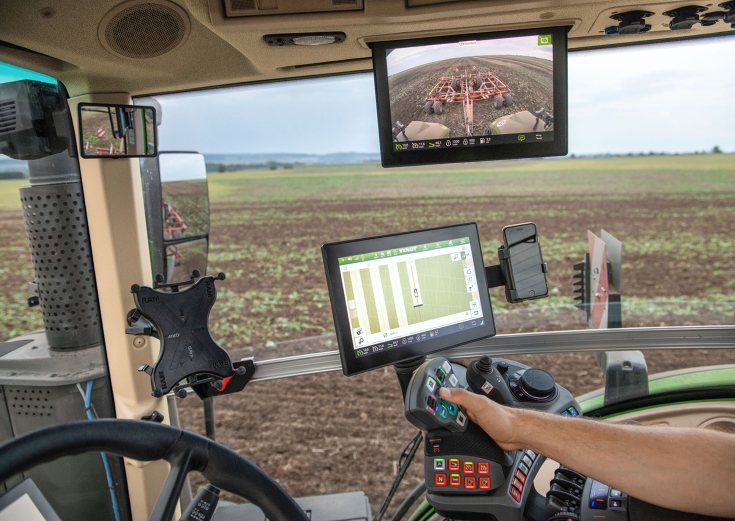 Innenraum der Fendt Kabine mit aktivierter Heckkamera und Spurführung. Eine Traktorenkabine von Innen mit Lenkrad und FendtONE Armlehne zur Traktorenbedienung inklusive Terminalanzeige für die Spurführung. Im Kabinendach ist ein weiterer Bildschirm verankert, dieser zeigt das Traktorenheck samt Grubber über eine Kamera, durc