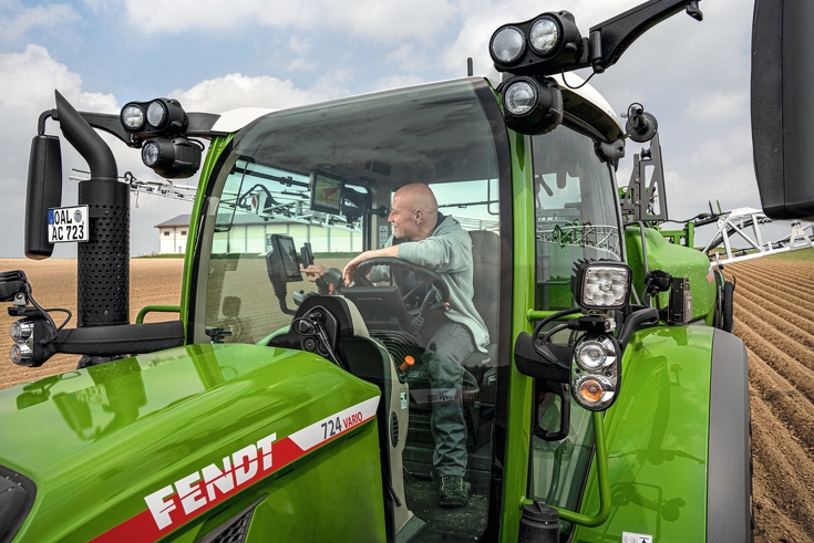 Man sitting in Fendt 724 Vario looking at FendtONE terminal and driving through a field