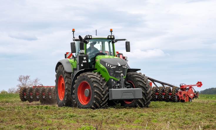 Fendt 1000 Vario driving in a field in overcast weather with mounted implement
