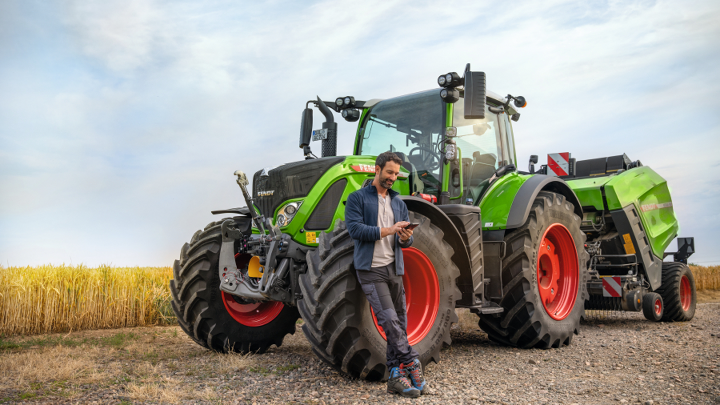 A farmer leaning onto his Fendt tractor having an online look onto the Fendt product overview website