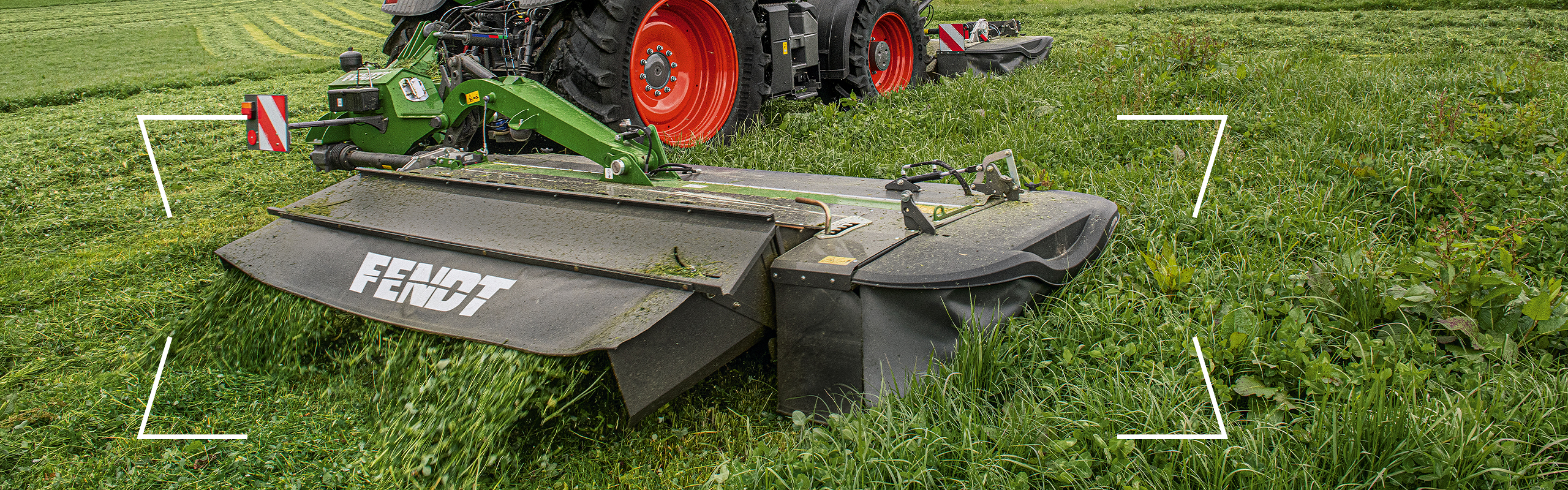 Rear-mounted Fendt Slicer Green Fendt tractor with red rims and rear-mounted Fendt Slicer in grassland during forage harvesting.