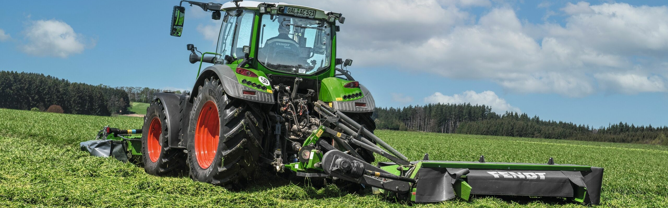 Fendt Slicer P Green Fendt tractor with red rims and rear-mounted Fendt Slicer P in grassland during forage harvesting.