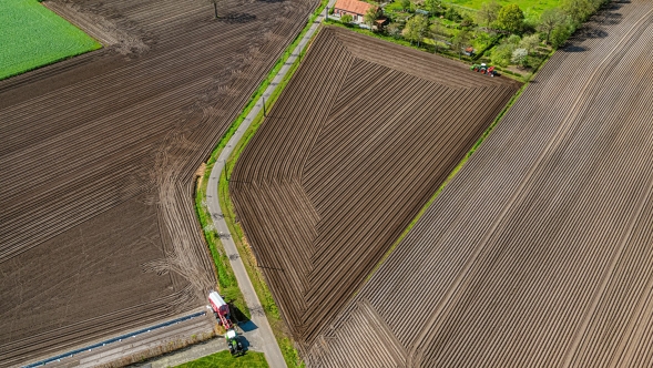 Fendt Section Control A Fendt tractor is driving out of a field. From a bird's eye view, you can see the fields that have already been worked with track guidance.