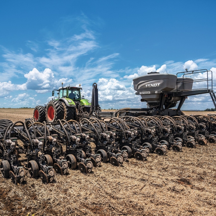 A Fendt Tractor with the Fendt Momentum Planter is driving on a field. In the background is the blue sky.