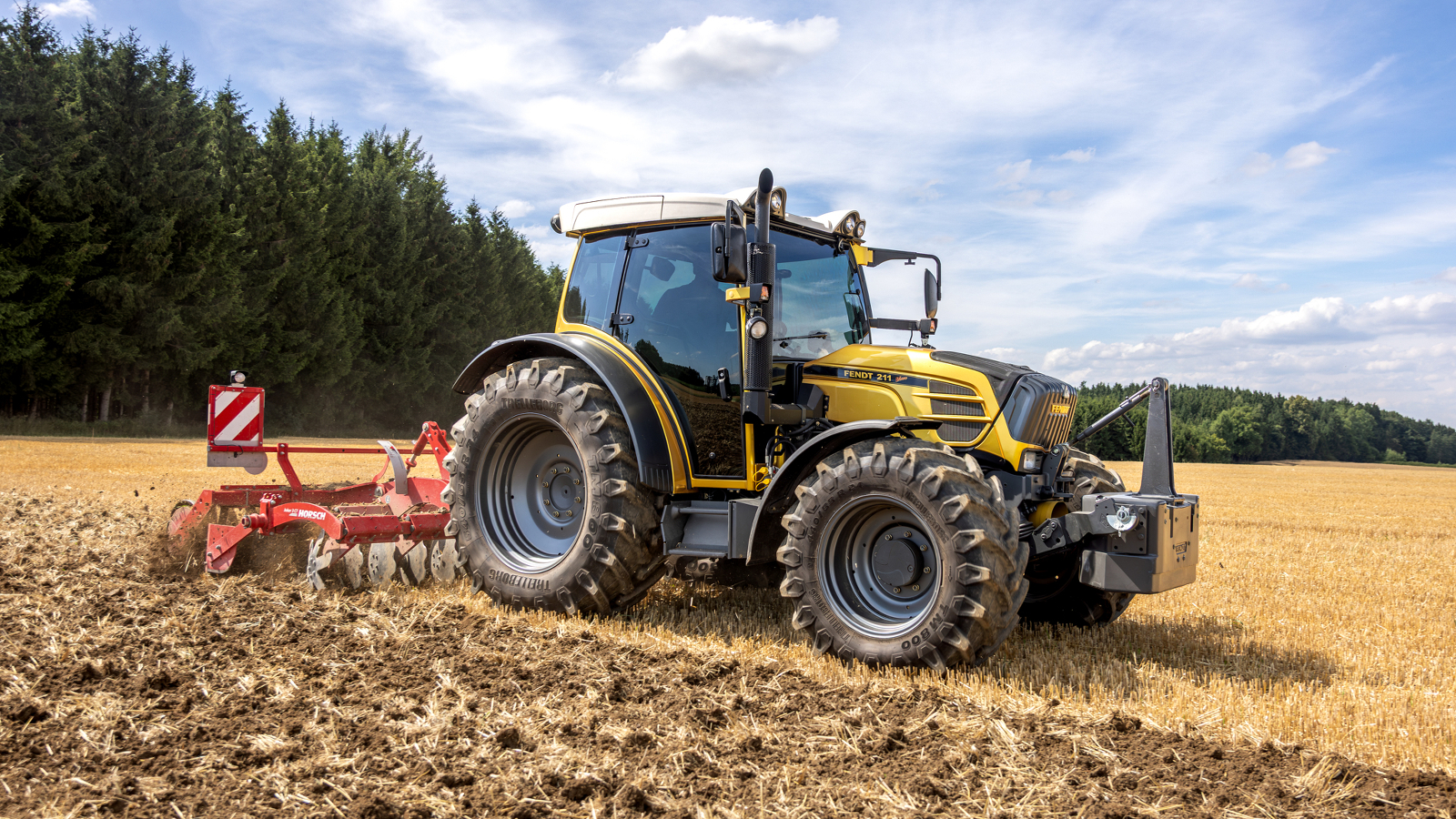 A golden Fendt 200 Vario standing in a field, in the background is a forest