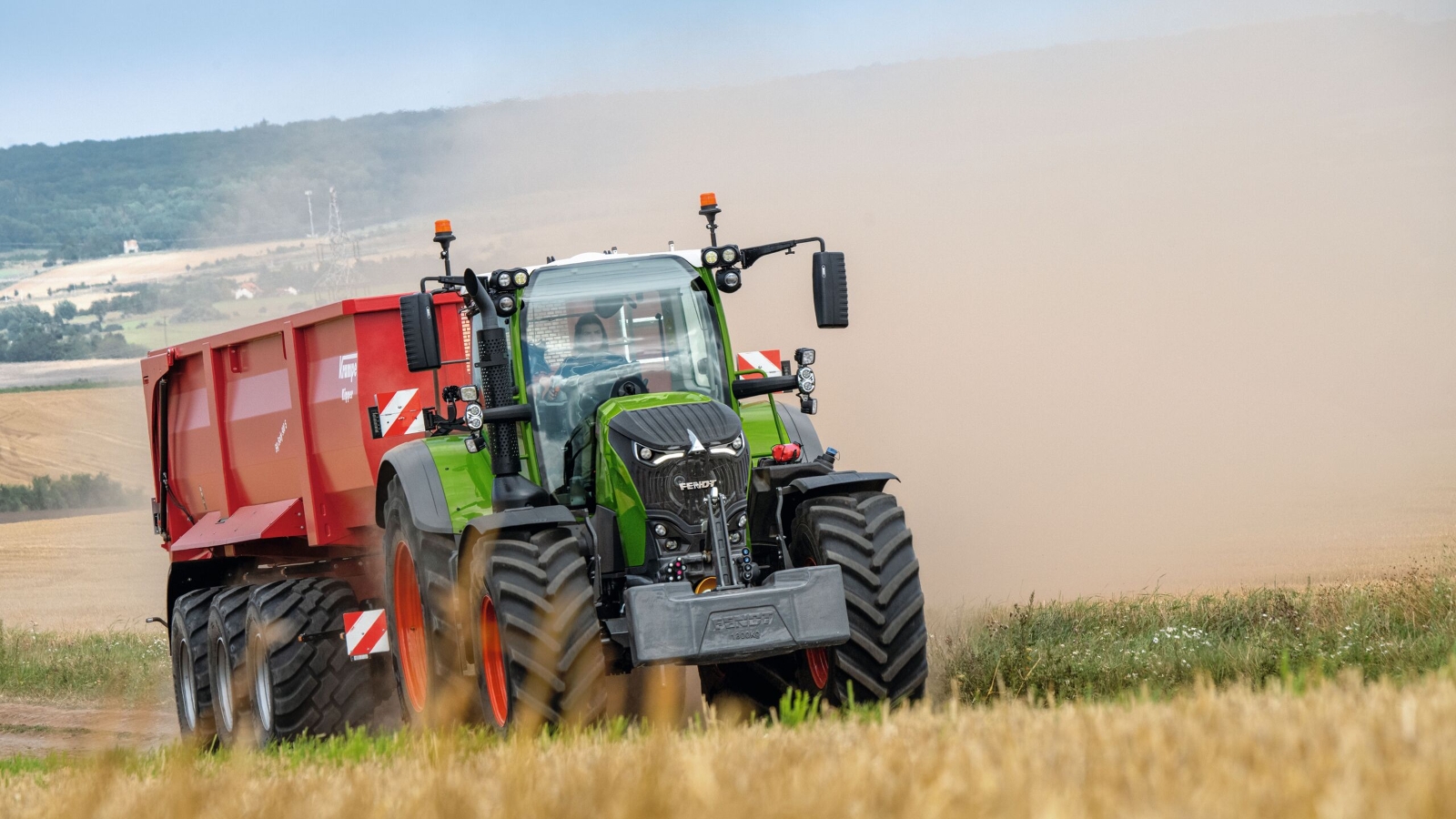 A farmer driving with a Fendt 700 Vario Gen7 and a red tipper in a field.