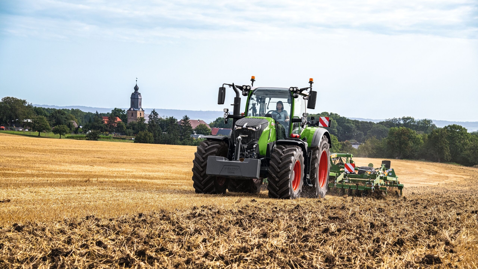A farmer driving a Fendt 700 Vario Gen7 and a cultivator in a field.