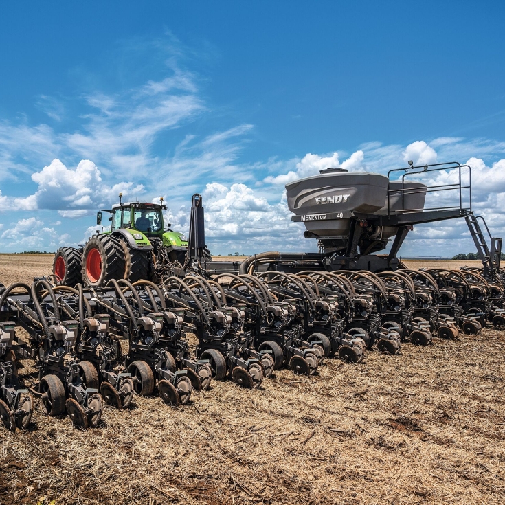 Um trator Fendt com a plantadeira Fendt Momentum está dirigindo em um campo. Ao fundo, o céu azul.